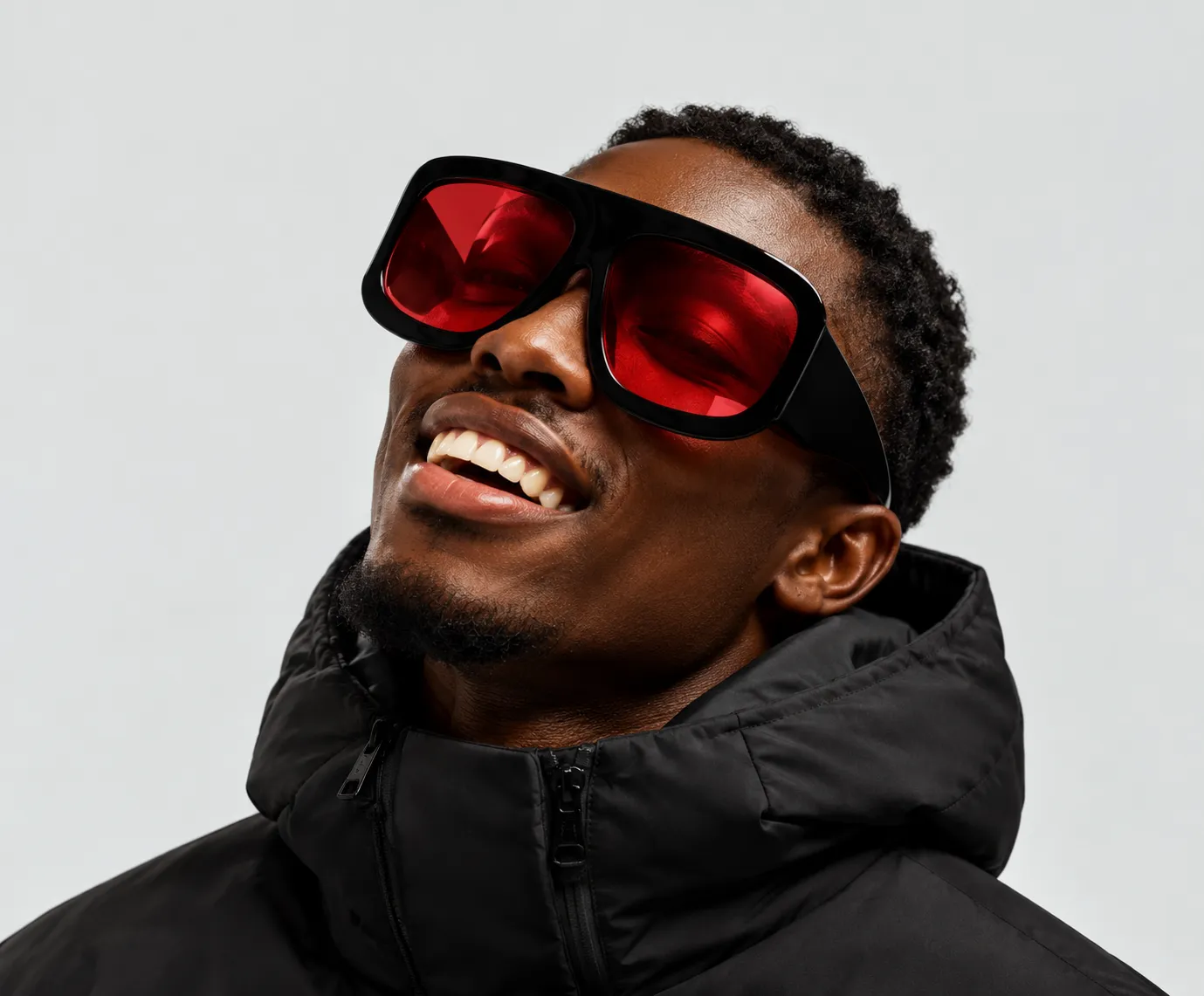 Smiling man in oversized red-lens sunglasses and a black puffer jacket